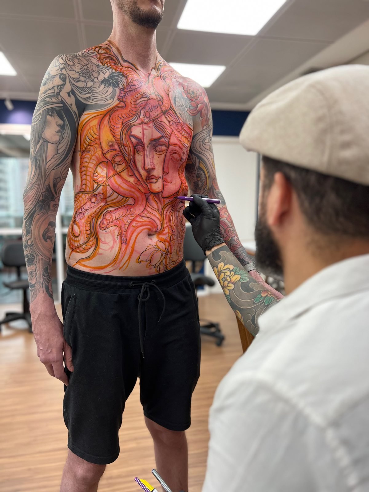 Denis Vazios desenhando freehand no torso de um cliente em pé