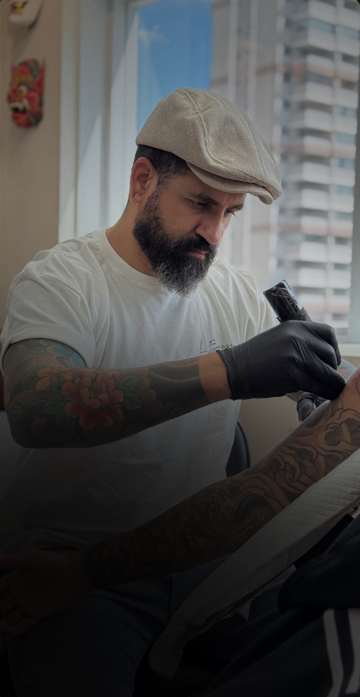 Denis Vazios tatuando o braço de um mentorado junto à janela do studio